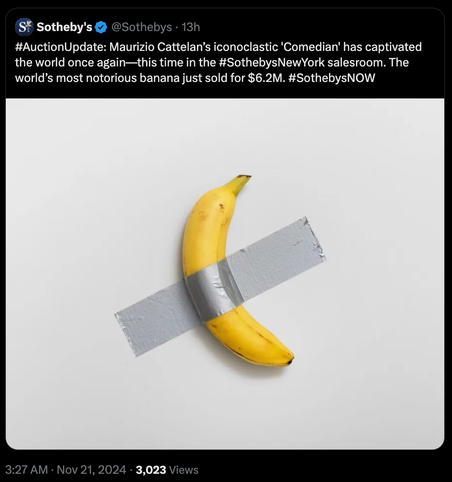A yellow banana with duct tape wrapped around it in an X-shape, photographed against a plain white background. The image is…
