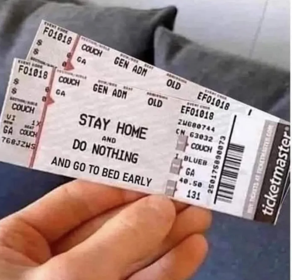 A hand holds two Ticketmaster event tickets that have been humorously altered with the text 'STAY HOME AND DO NOTHING AND GO…