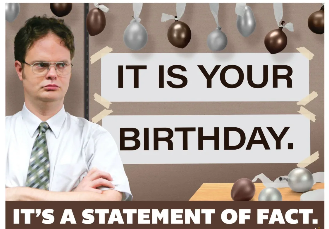 A man in a white shirt and tie with arms crossed stands in front of a bulletin board decorated with brown and silver…