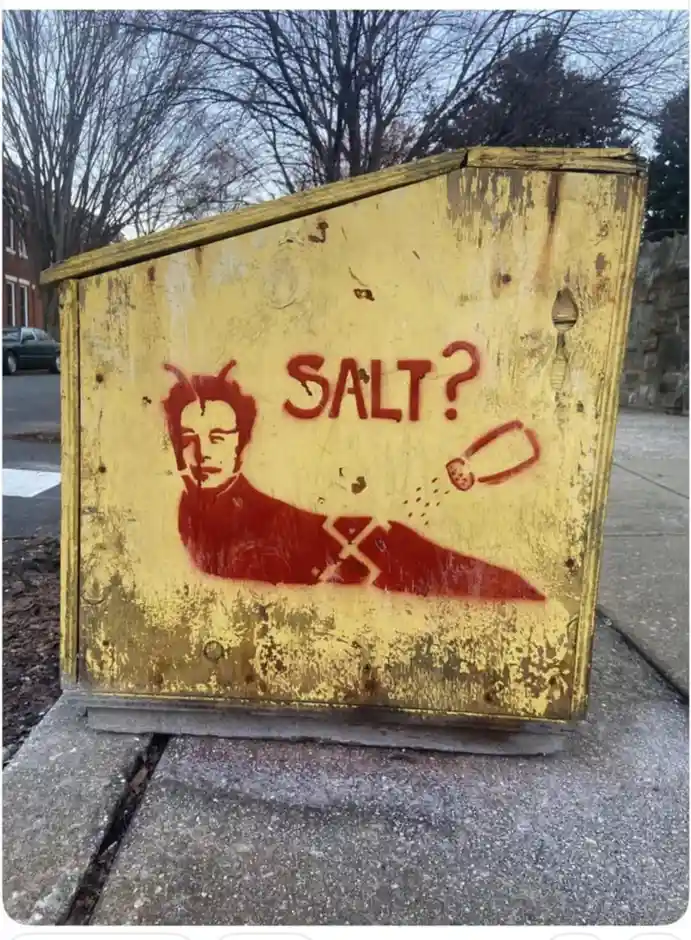 A weathered yellow wooden box, likely an old utility or electrical cabinet, is spray-painted with a red stencil. The stencil…