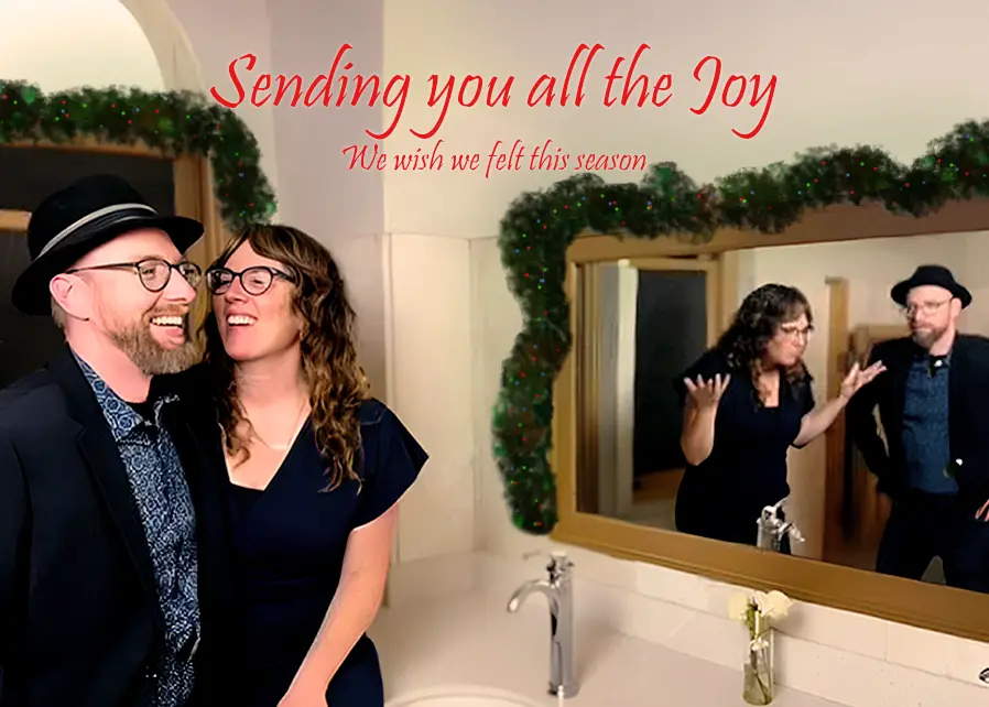 A man and woman in a bathroom smile happily at each other while their reflection in the mirror shows them looking annoyed…