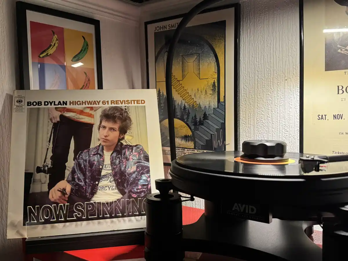 A vinyl record player with a record on it sits next to the album cover for Bob Dylan's 'Highway 61 Revisited', which has the…
