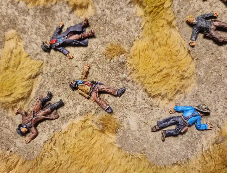Several small, painted toy figures dressed in Western-style clothing lie motionless on a textured surface that resembles a…