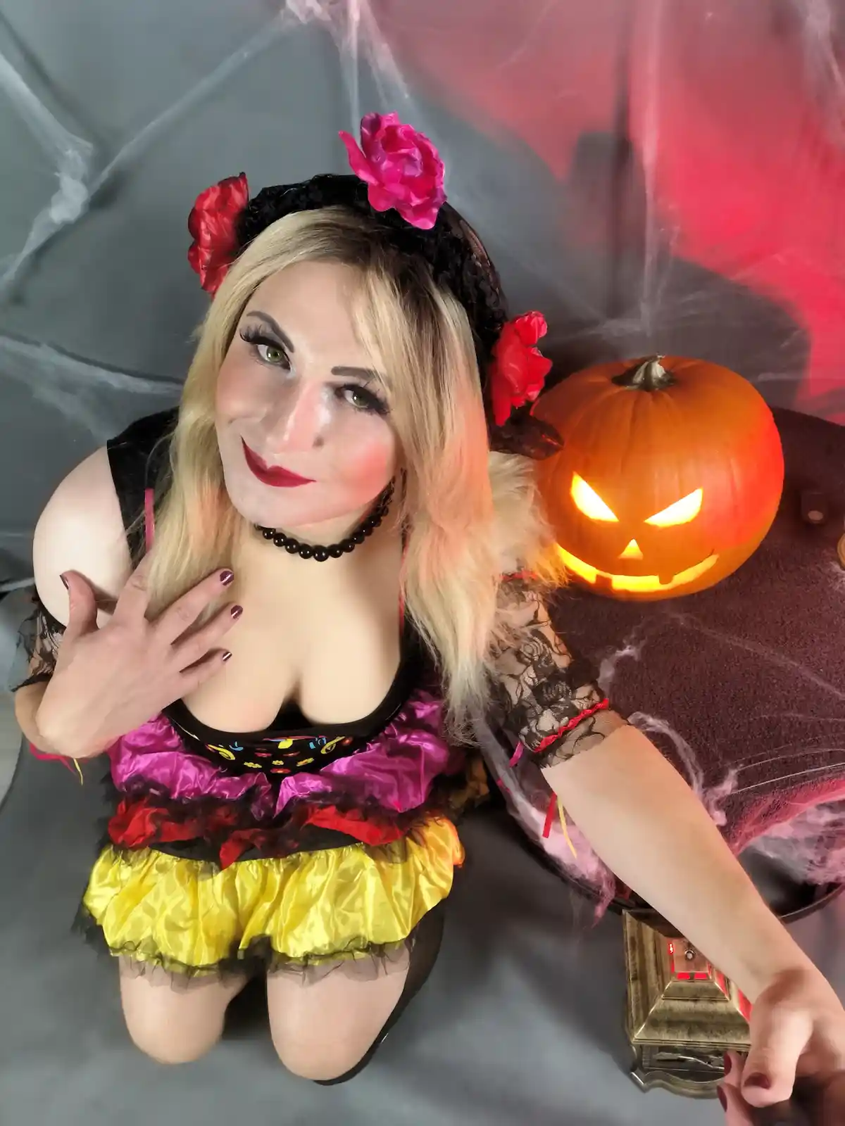 A woman in a colorful Halloween costume with a black lace headband adorned with red and pink flowers kneels beside a lit…