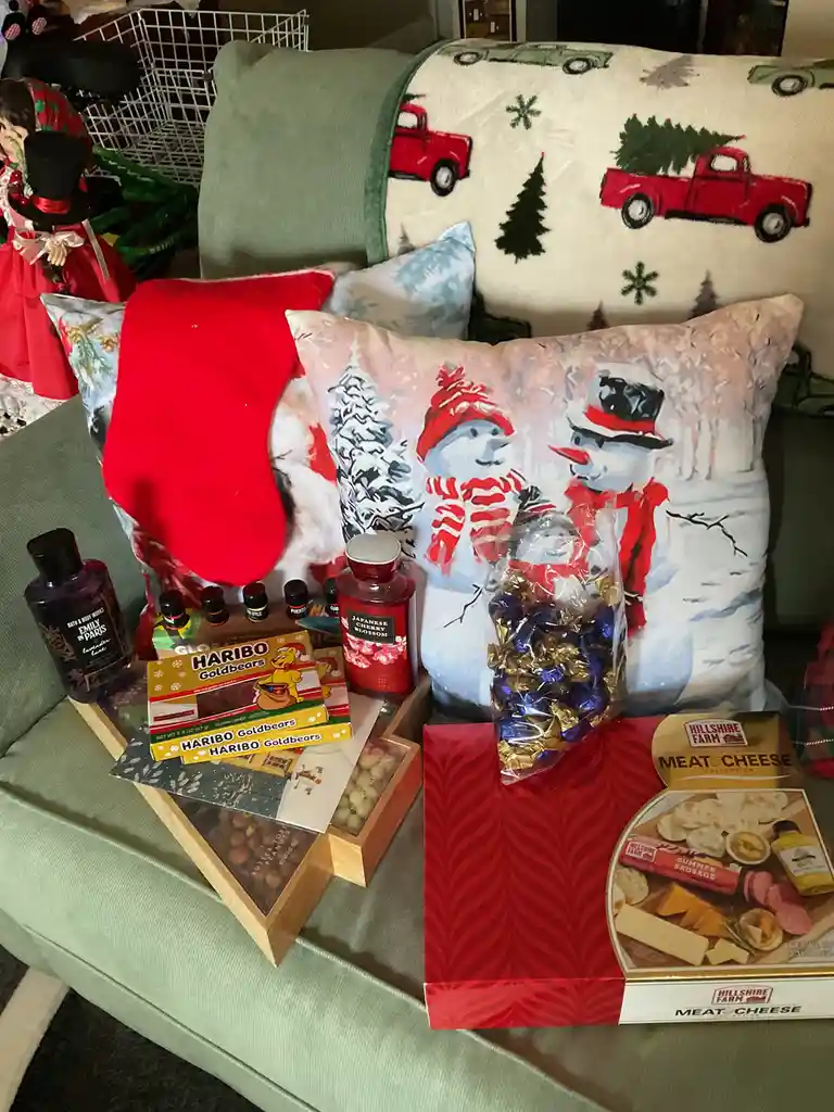 A green couch is covered with christmas-themed items including snowman pillows, a red stocking, and a blanket with red…
