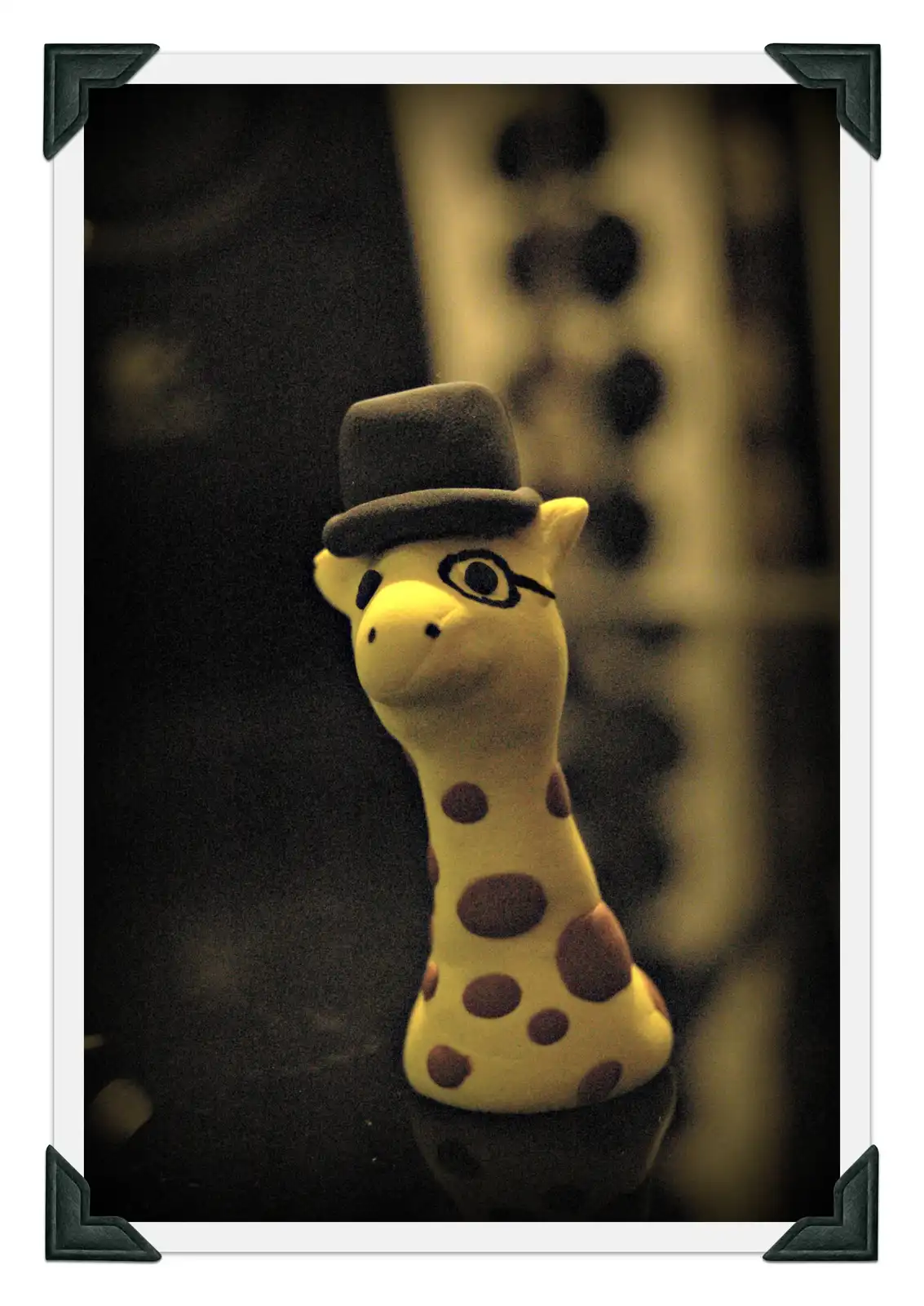 A close-up photo of a plush giraffe toy wearing a black top hat and black-rimmed glasses, set against a dark, blurred…