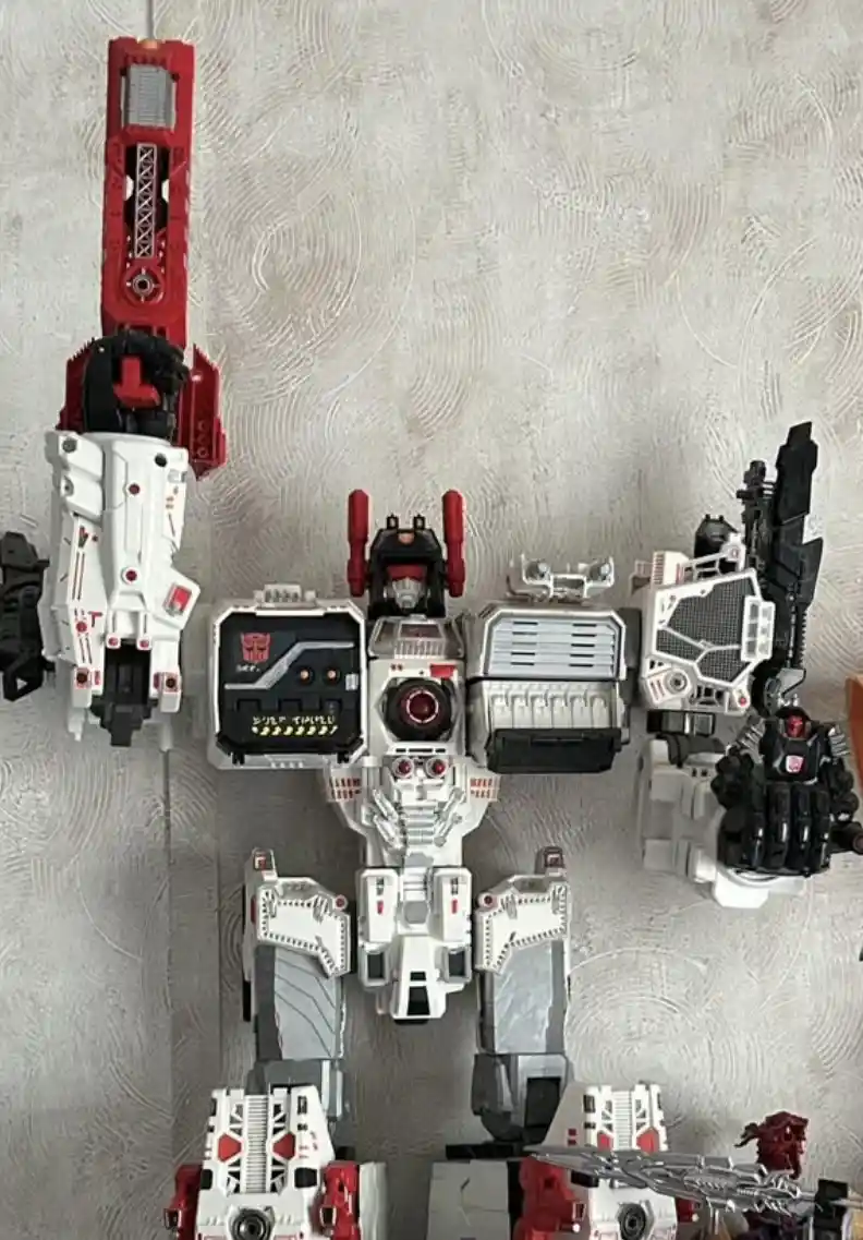 A large white and red Transformers toy robot is laid out on a textured gray surface, with its arms and legs spread out. The…