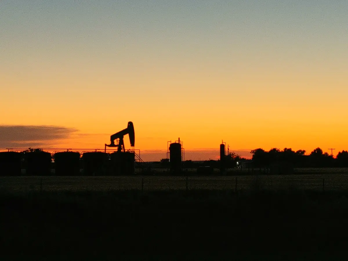A silhouette of an oil pumpjack and storage tanks against a vibrant orange and blue sunset sky. The overlaid text reads 'i'm…