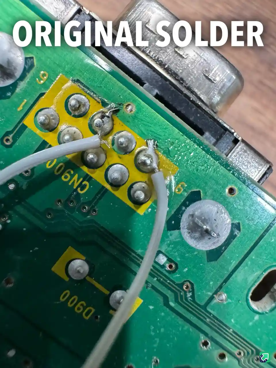 A close-up photo of a green circuit board with a yellow connector area, showing several solder joints. A white wire is…