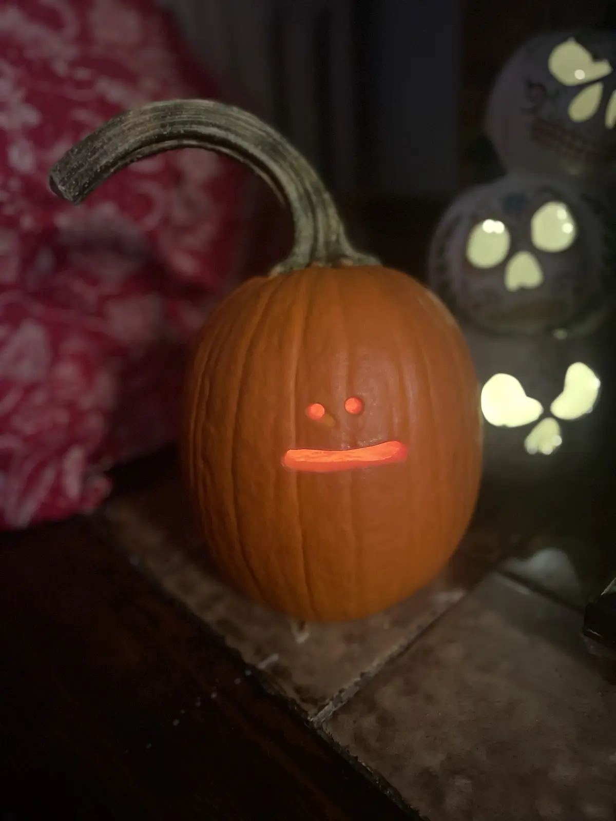 A carved orange pumpkin with a lit interior, featuring a simple face with two small round eyes and a straight horizontal…