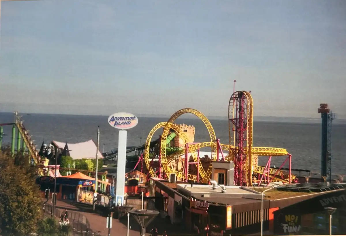 A wide-angle photograph of Adventure Island amusement park, featuring a large yellow roller coaster with loops and a red…