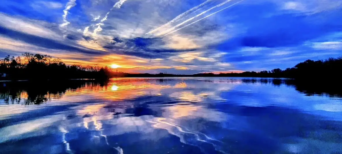 A serene sunset over a calm lake, with vibrant orange and blue skies reflected in the water, overlaid with the text 'i'm not…