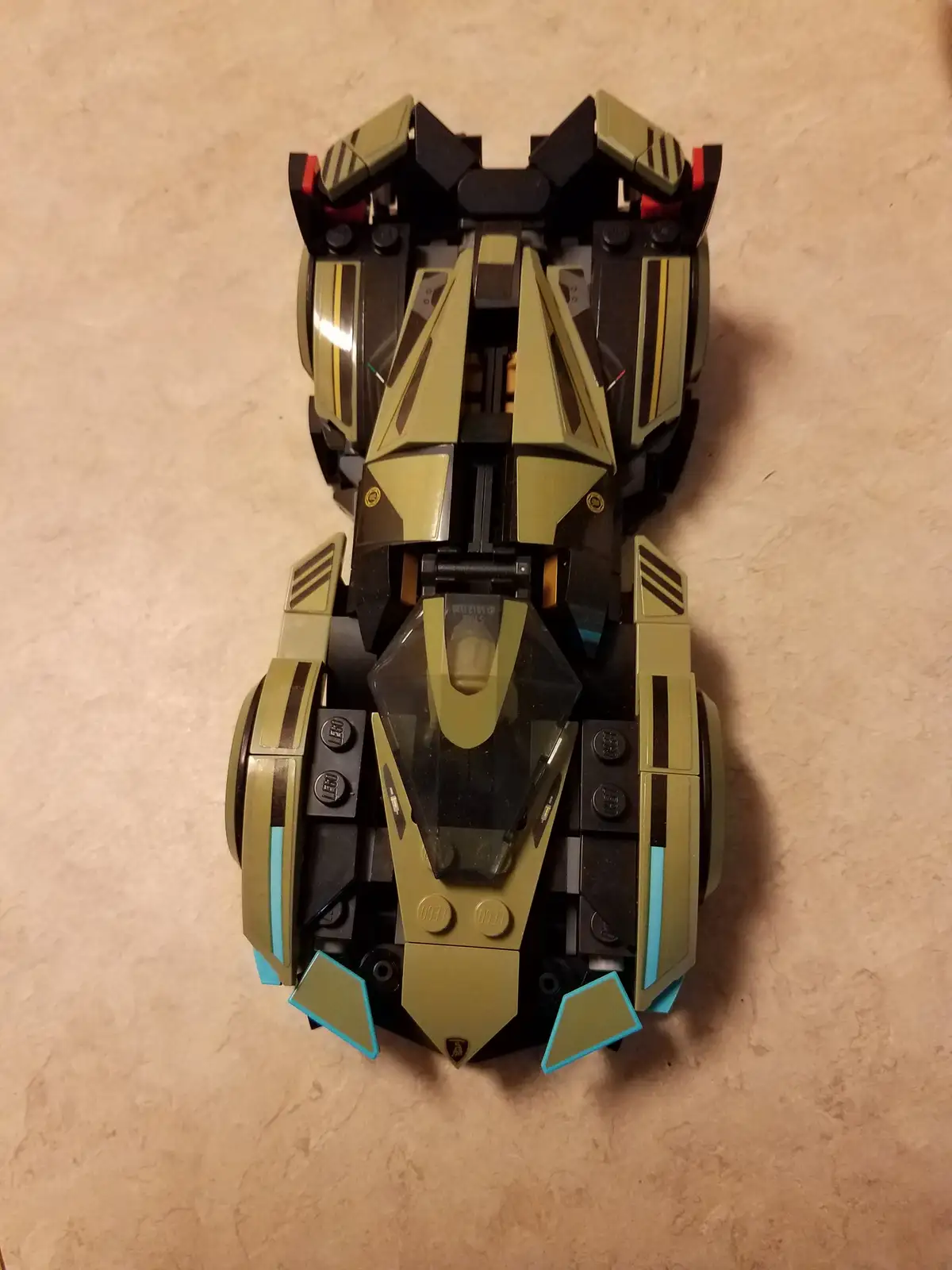A top-down photograph of a Lego Batmobile, showcasing its symmetrical black and gold design with teal accents on the front…