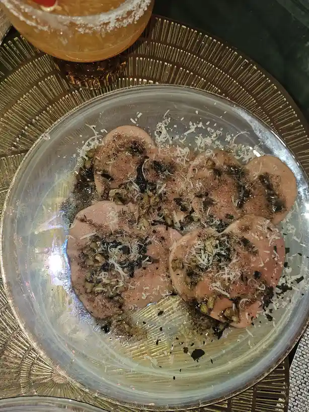 a clear glass plate holds four pink, brain-shaped food items topped with shredded cheese, chopped nuts, and dark seasoning…