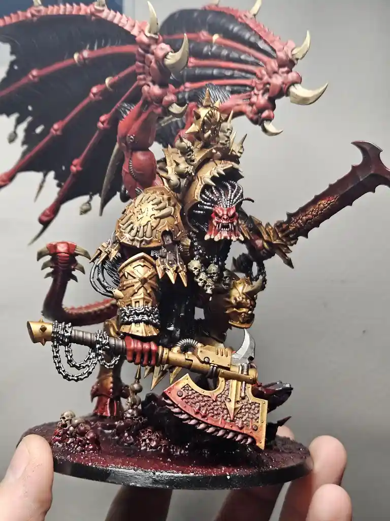 A highly detailed, painted miniature of a demonic warlord with red and black wings, multiple horns, and ornate golden armor…