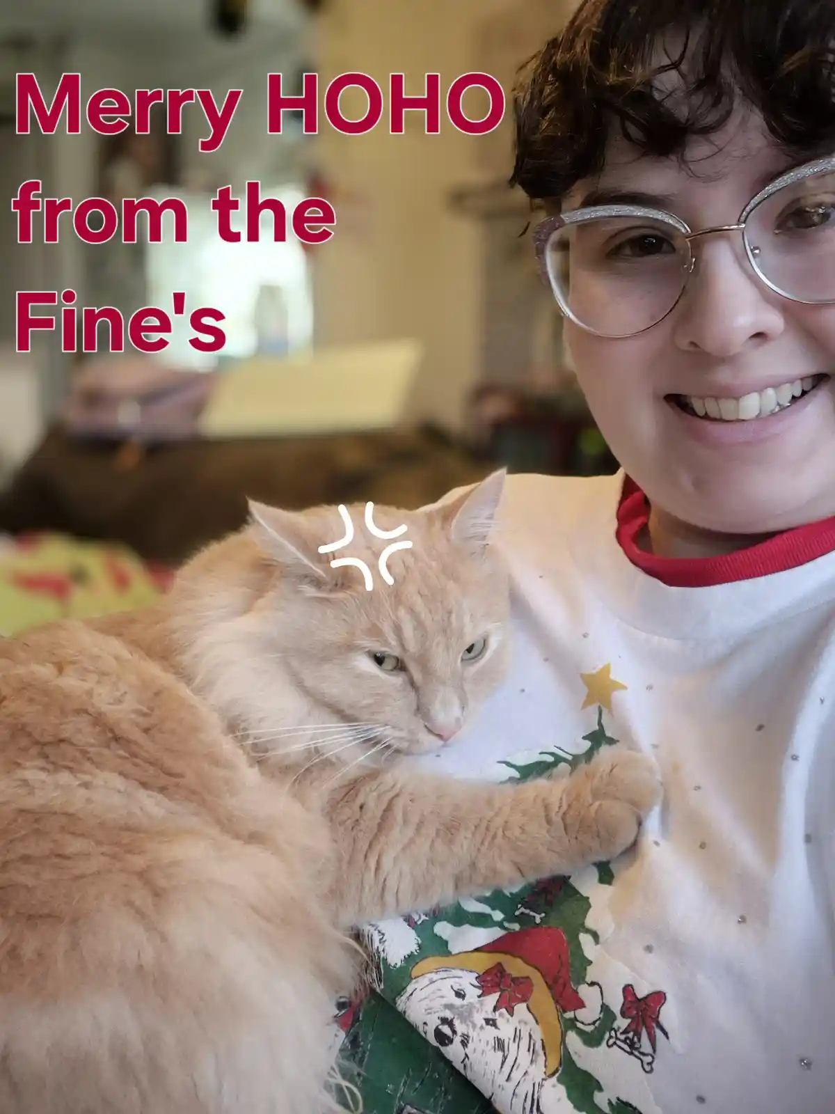 A person with curly hair and sparkly glasses smiles while wearing a festive Christmas sweater and holding a fluffy orange…