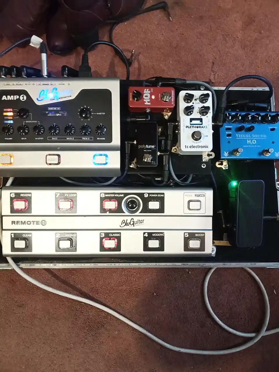 An overhead shot of a complex guitar pedalboard setup featuring a BluGuitar amp modeler, multiple effects pedals including a…