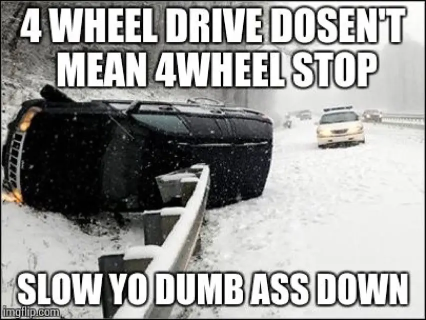 A black SUV is flipped upside down in a snowy ditch next to a guardrail, with a police car visible in the background on a…