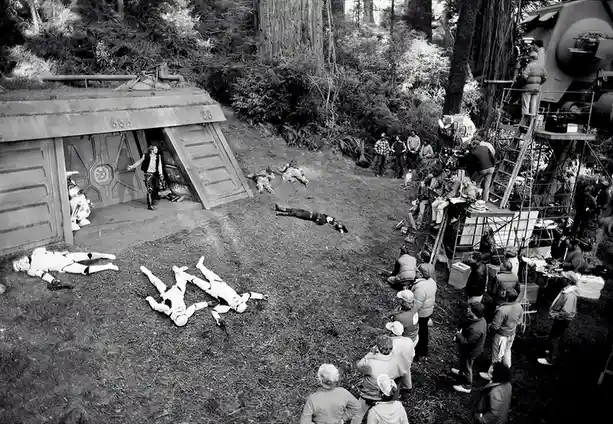 A black-and-white behind-the-scenes photograph from a Star Wars film set, showing Harrison Ford as Han Solo standing in the…
