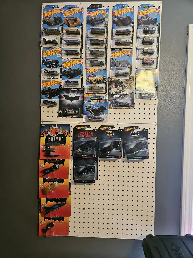 A white pegboard wall displays dozens of Hot Wheels and other Batman-themed toy car packages, mostly featuring various…