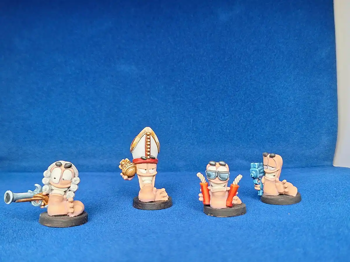 Four painted figurines of the cartoon character Garfield are arranged in a row on a blue felt surface. From left to right…