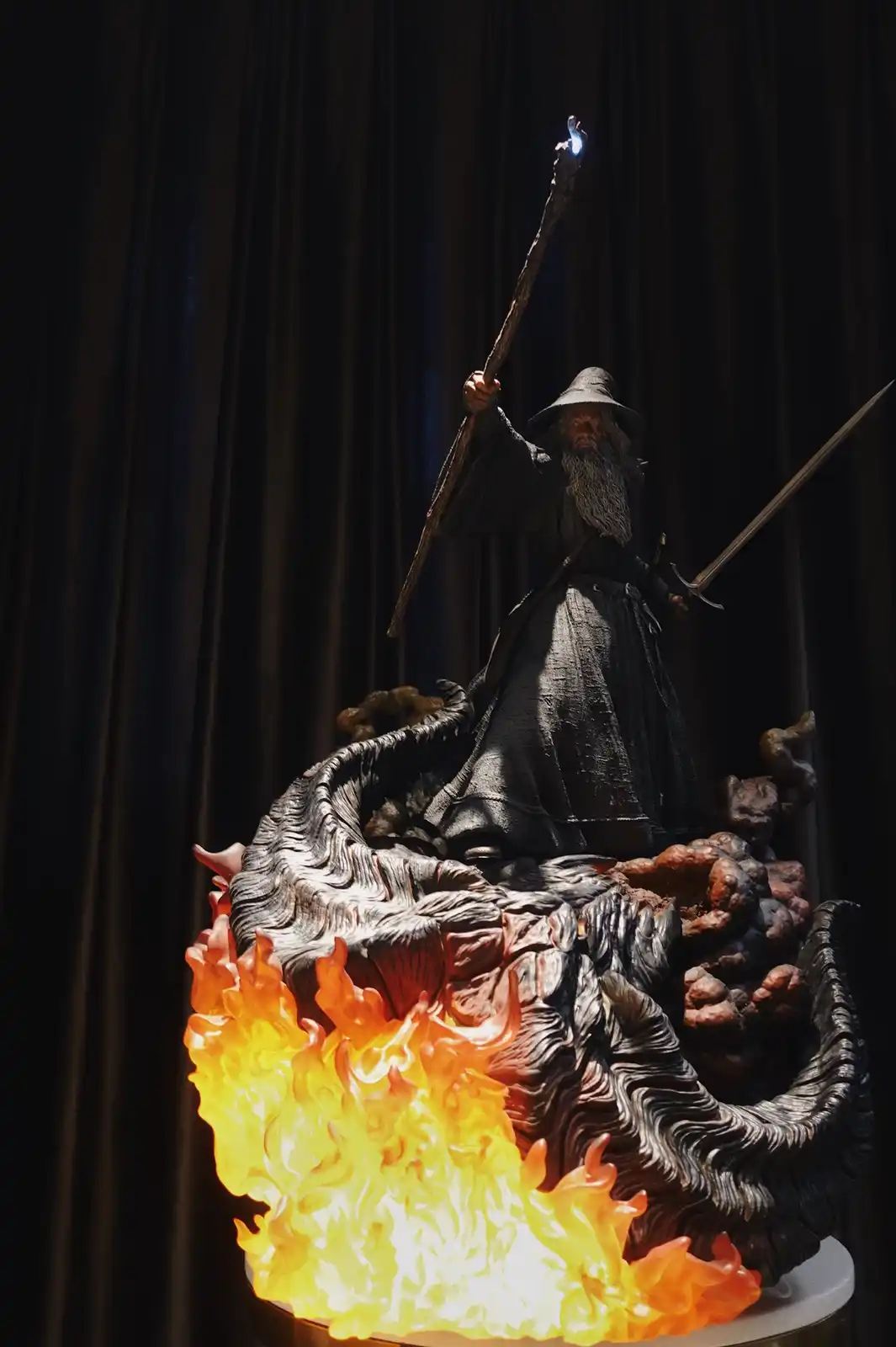 A highly detailed statue of Gandalf the Grey from Lord of the Rings stands atop a sculpted, fiery dragon-like base, holding…