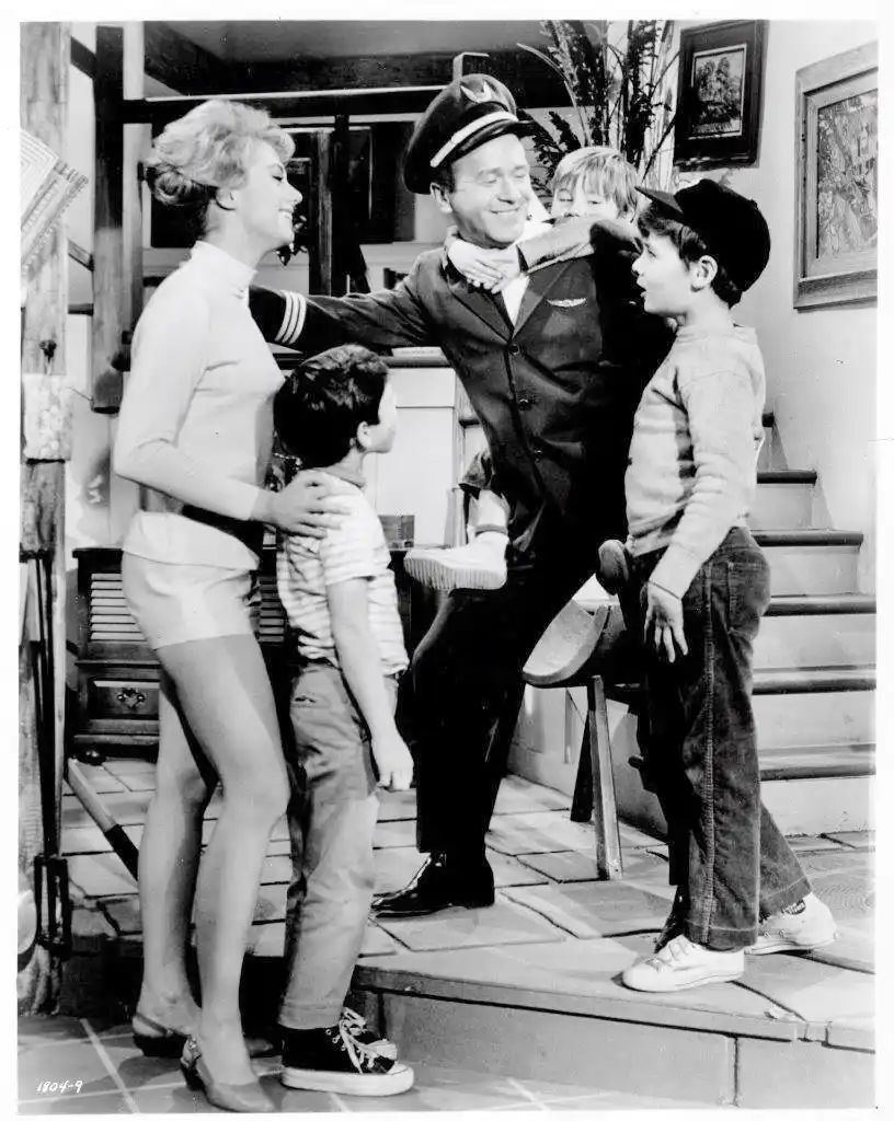 A black-and-white photo from the 1960s TV show 'Bewitched' shows a man in a pilot's uniform smiling while holding a young…