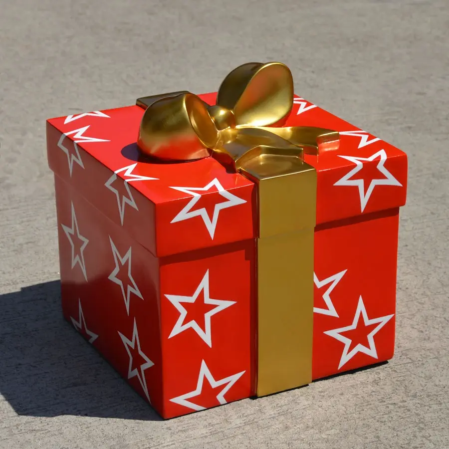 A large, red, box-shaped gift with white stars and a gold ribbon bow sits on a gray pavement. The overlaid text reads 'i'm…