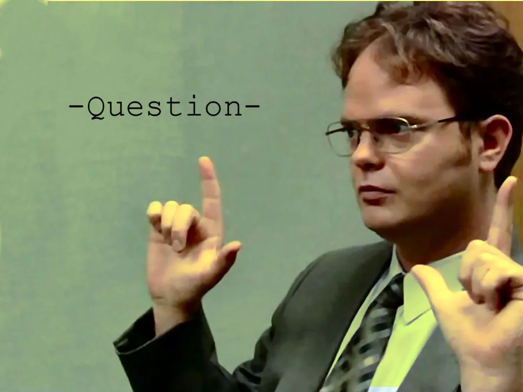 A man in a suit and glasses, identified as Dwight Schrute from The Office, points both index fingers upward with a serious…