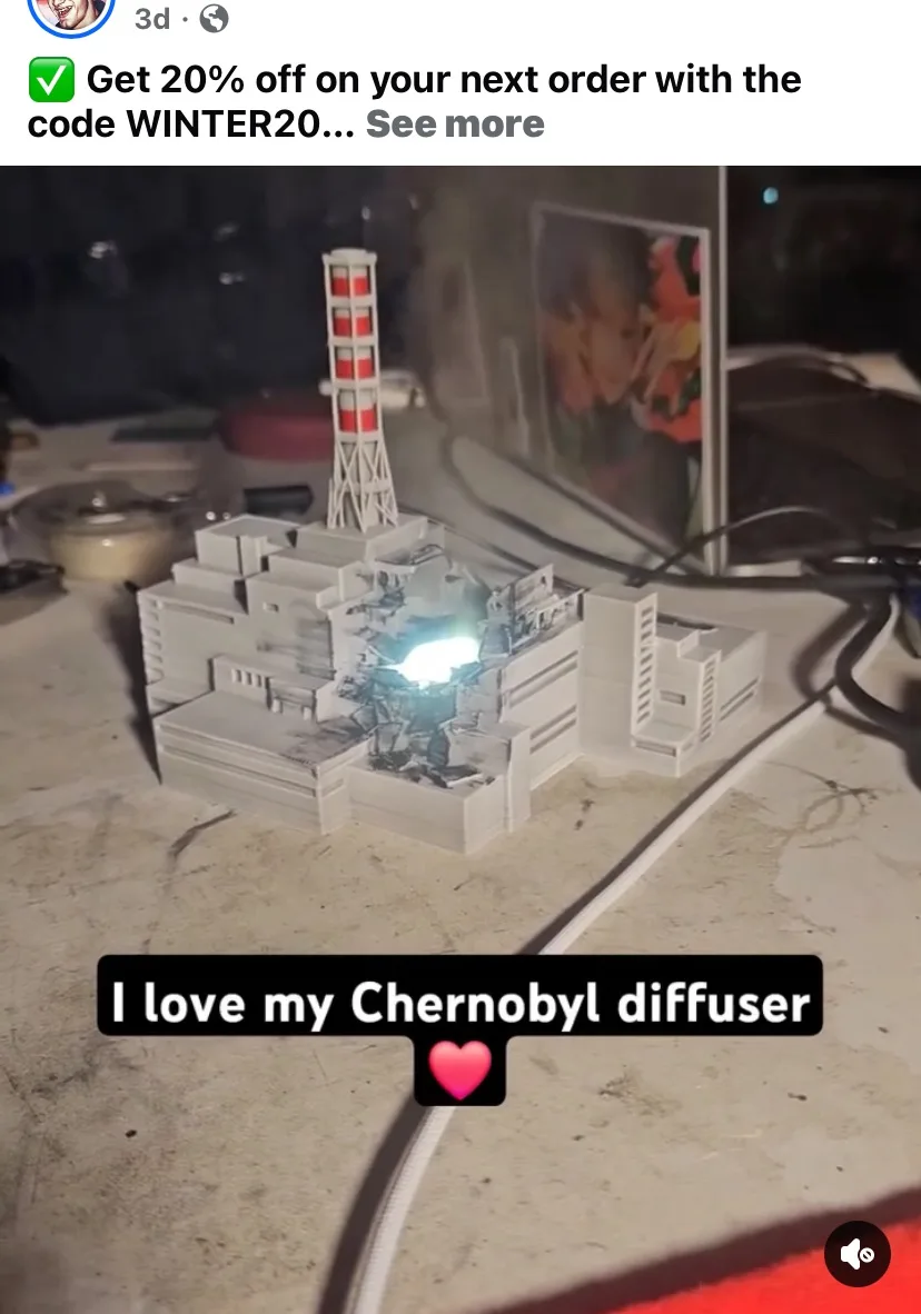 A 3D-printed model of the Chernobyl nuclear power plant is shown on a cluttered desk, with a bright light glowing from its…