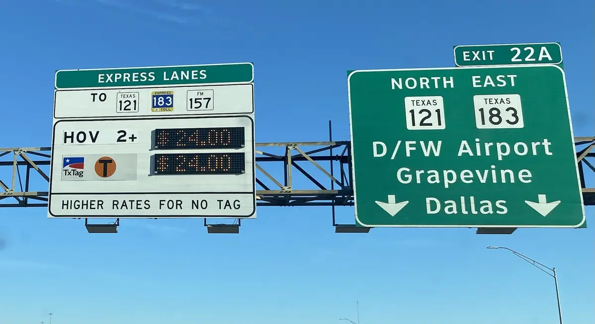 A highway sign for Texas express lanes shows HOV 2+ tolls at $24.00 for both TxTag and non-tag users, with a warning that…