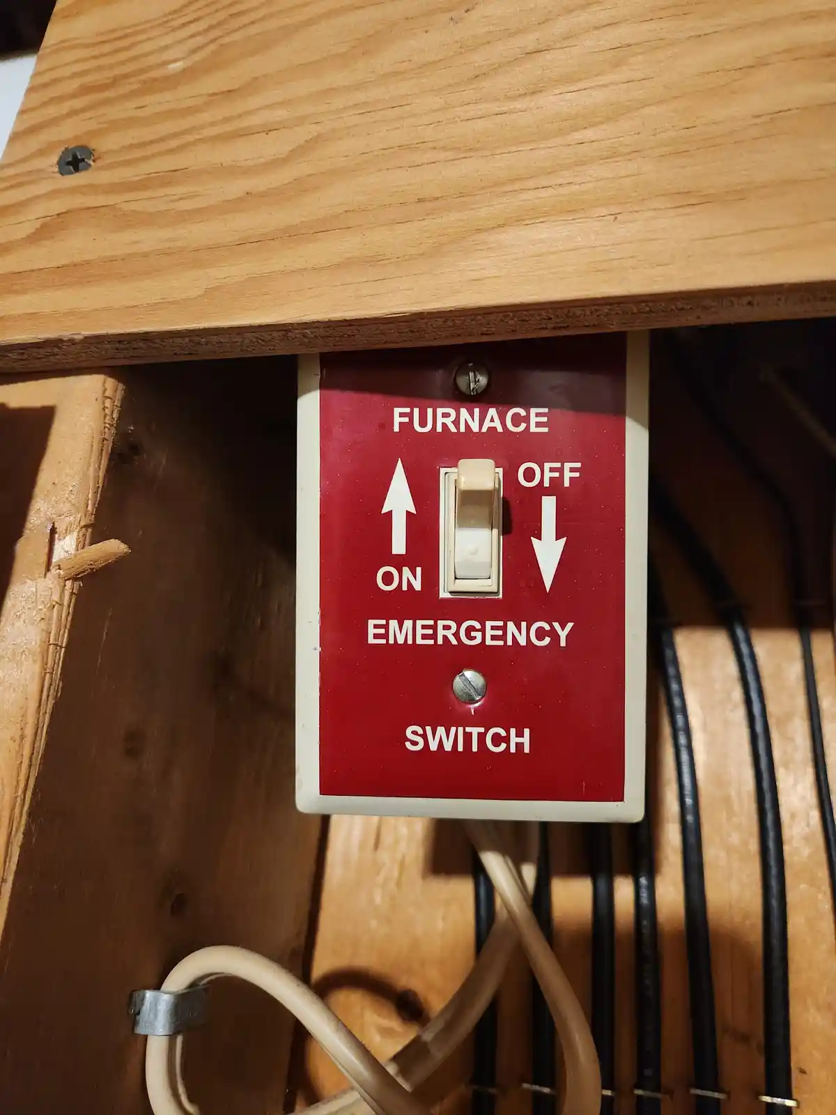 A close-up of a red-labeled furnace emergency switch mounted on wood, with a toggle switch positioned between 'ON' (up…