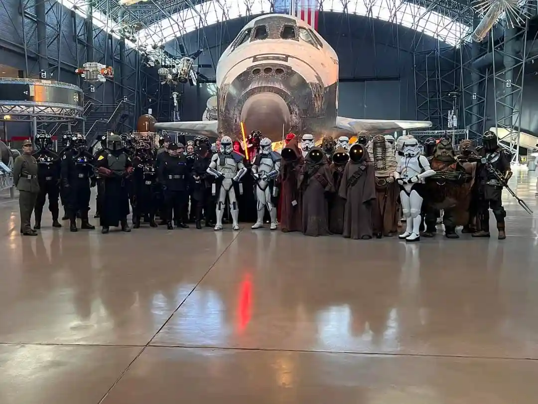 A group of people dressed as Star Wars characters, including stormtroopers, jedis, and aliens, pose for a photo in front of…
