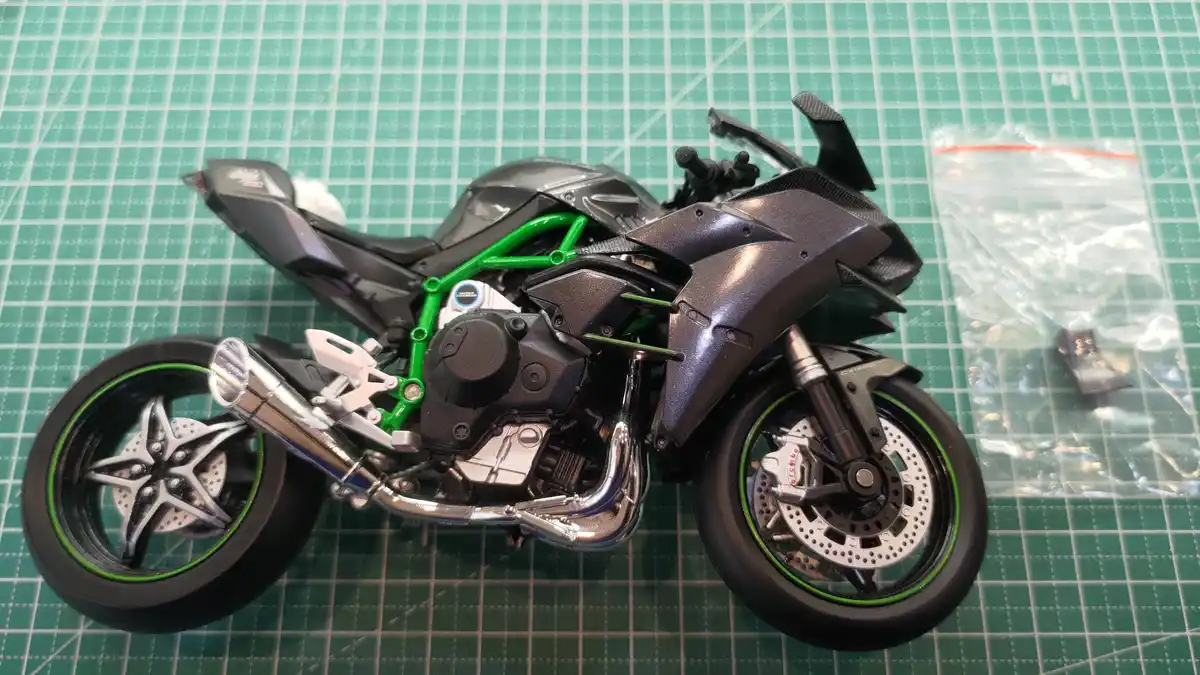 A detailed scale model of a black and green sport motorcycle with chrome exhaust and visible suspension, sits on a green…