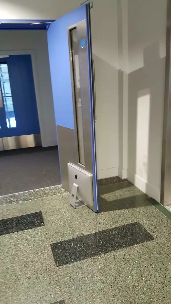A modern blue door with a silver handle is slightly ajar, revealing a silver Apple iMac computer wedged in the bottom of the…