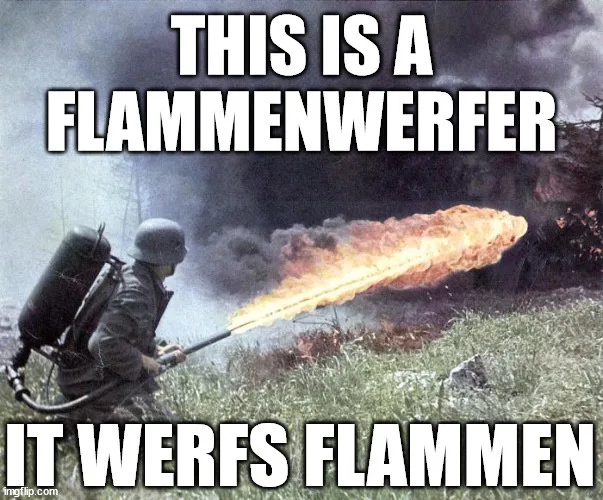 A soldier in a helmet and military uniform is operating a flamethrower, spraying a long stream of fire across a grassy field…