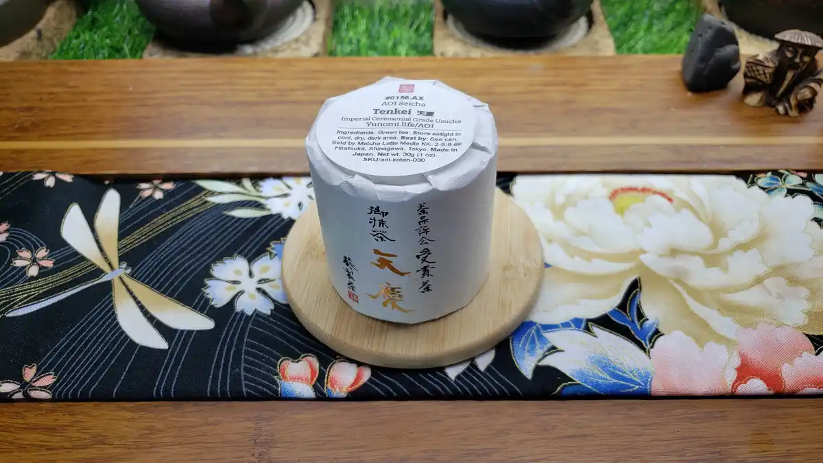 A cylindrical, white-wrapped Japanese green tea container labeled 'Tenkei 天慶 Imperial Ceremonial Grade Usucha' sits on a…