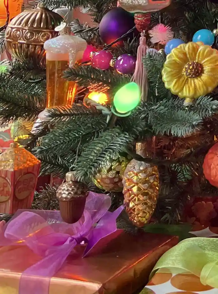 A close-up of a decorated christmas tree with colorful ornaments including a glittery golden pinecone, a cupcake, a popcorn…