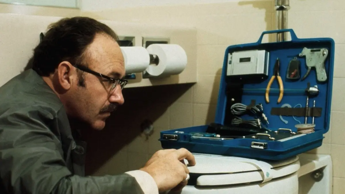 A man with glasses and a mustache is in a bathroom, looking intently at a blue toolbox filled with various tools and…