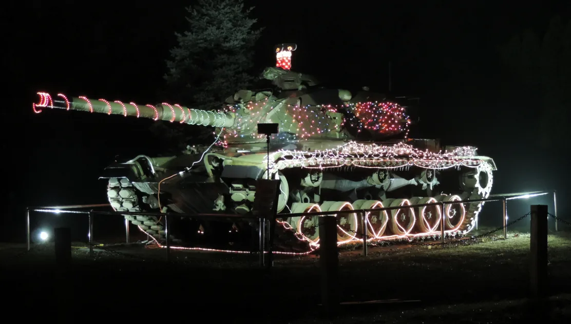 A military tank is decorated with colorful Christmas lights at night, with red and white lights outlining its turret…