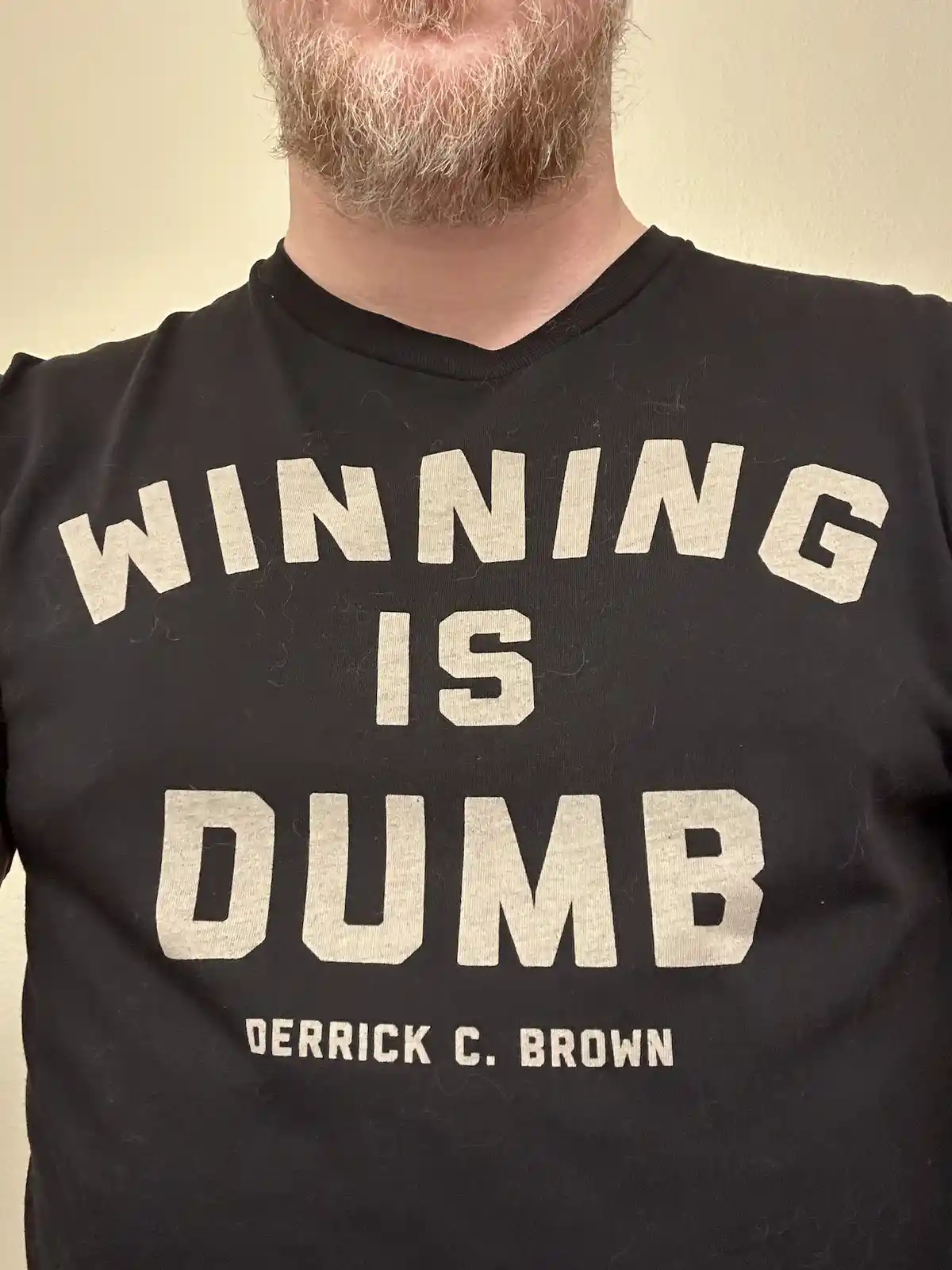 A close-up shot of a man's chest wearing a black t-shirt with large, white, blocky text that reads 'WINNING IS DUMB' and…