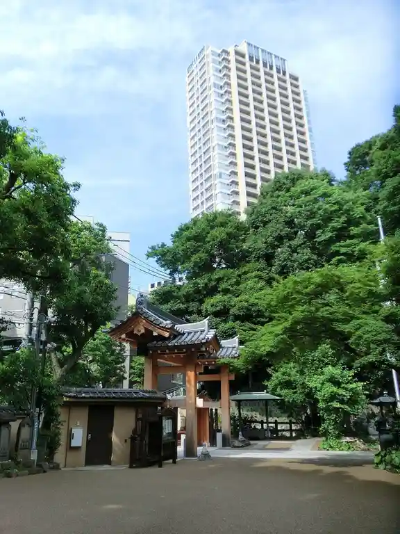 a traditional wooden torii gate of a japanese temple is framed by lush green trees, with a modern high-rise apartment…