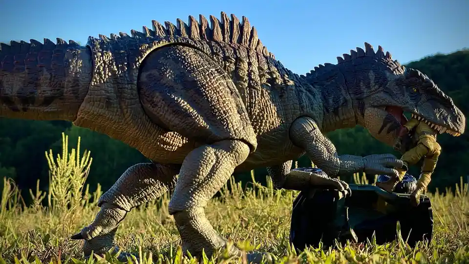 A large, detailed plastic dinosaur toy with a spiked back and textured skin is shown outdoors in grass, holding a smaller…