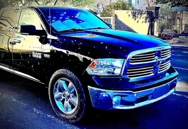 A black Ram 1500 pickup truck is parked in a driveway, its windshield decorated with blue stars resembling the american…