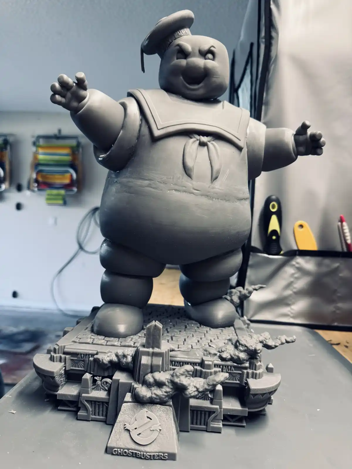 A gray, unpainted 3D-printed statue of the Ghostbusters character Slimer stands on a detailed base featuring the…