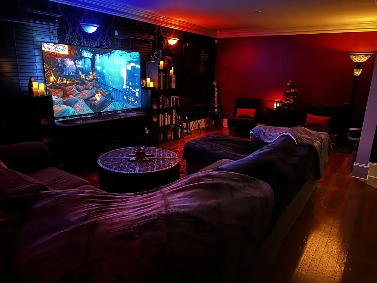 A dimly lit, cozy room with red and blue ambient lighting, featuring two large beds covered in blankets, a large TV…