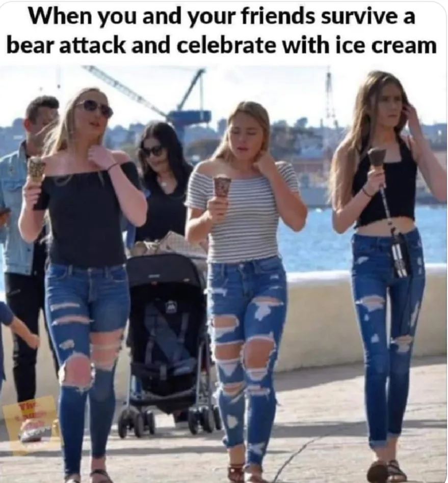 A group of young women, dressed in ripped jeans and casual summer clothes, are walking along a waterfront promenade while…