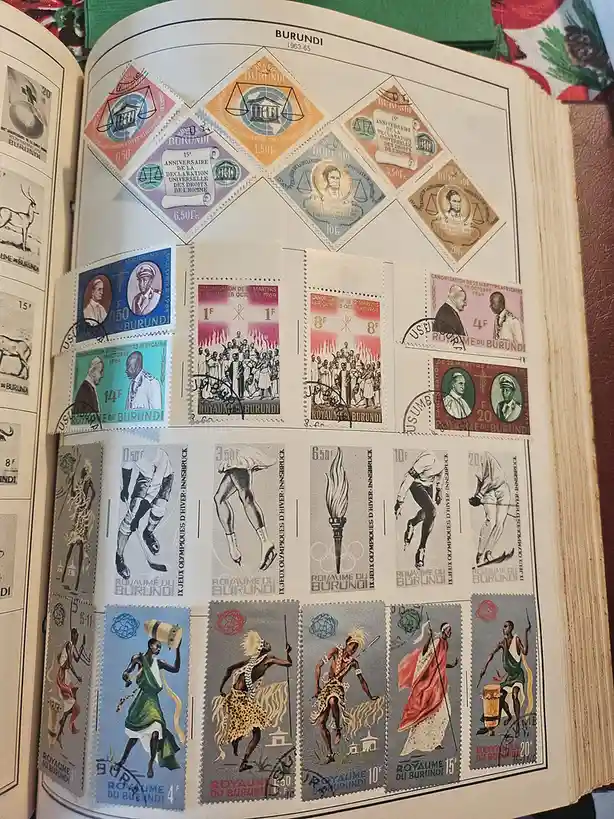 An open stamp album page displays a collection of Burundian postage stamps from the 1960s, featuring various themes…