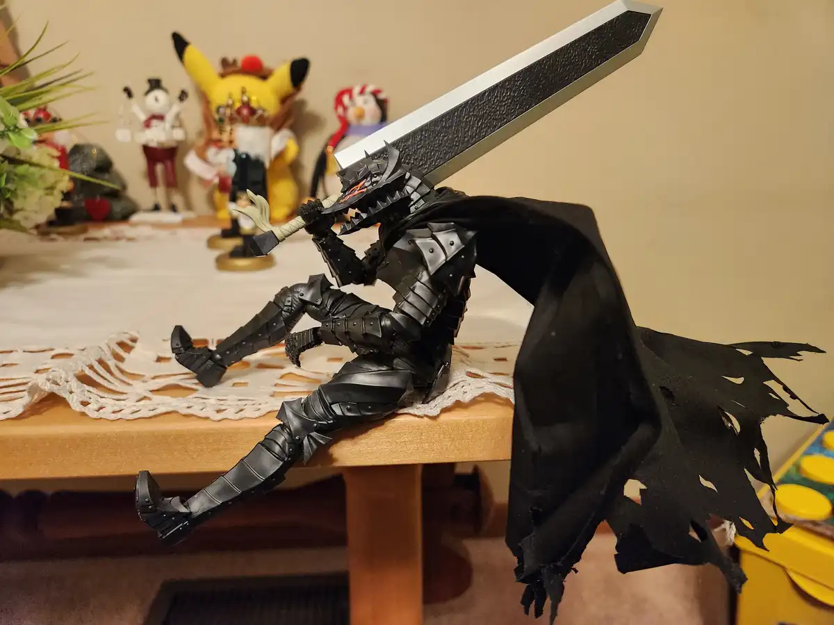 A black-armored action figure, resembling a knight or warrior with a large sword on its back and a tattered black cape, is…