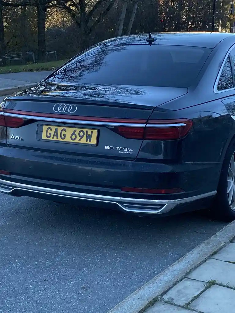 The rear view of a dark grey Audi A8L 60 TFSIe quattro parked on a street, showing its license plate which reads 'GAG 69W'…
